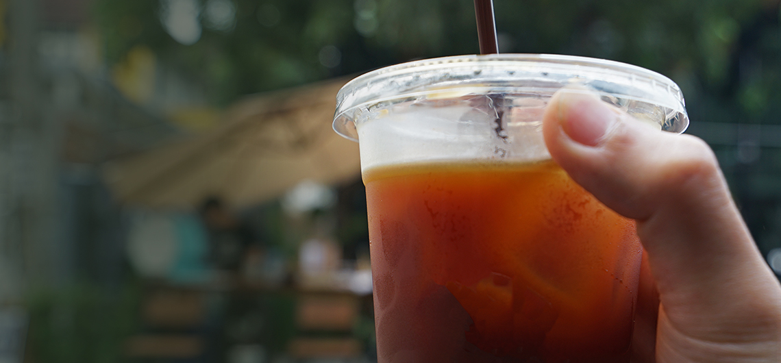 close-up of hand holding soft drink cup with lid and straw
