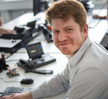 young redheaded man at his desk, smiling