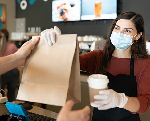 counter service, barista in mask hands bag and coffee to customer